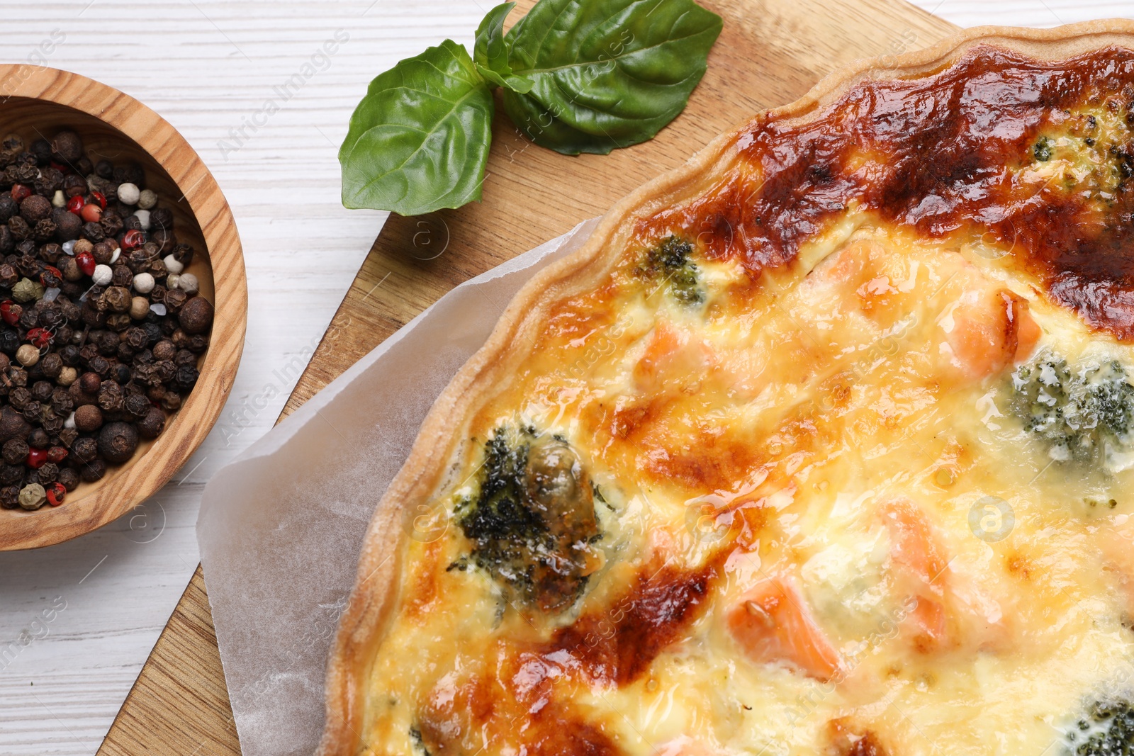Photo of Delicious homemade quiche with salmon, broccoli, basil leaves and spices on wooden table, flat lay
