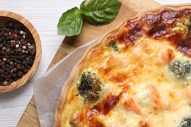 Delicious homemade quiche with salmon, broccoli, basil leaves and spices on wooden table, flat lay