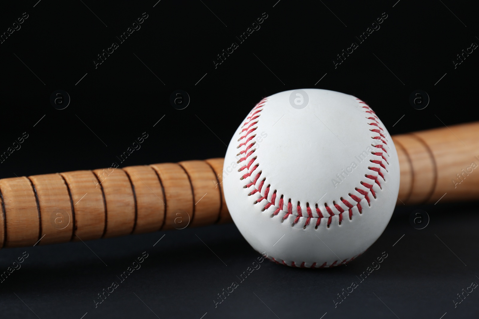 Photo of Wooden baseball bat and ball on black background, closeup. Sports equipment