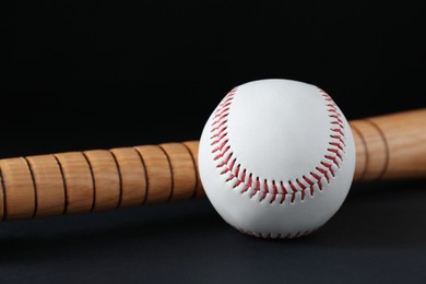 Photo of Wooden baseball bat and ball on black background, closeup. Sports equipment