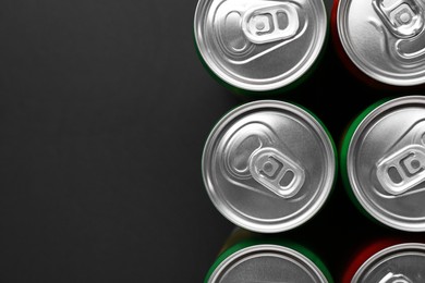 Energy drink in cans on black background, top view. Space for text