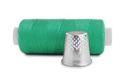 Photo of Thimble and spool of green sewing thread isolated on white