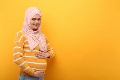 Portrait of pregnant Muslim woman in hijab on orange background, space for text