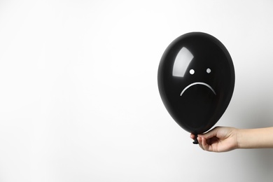 Photo of Woman holding balloon with sad face on white background, space for text. Threat of depression