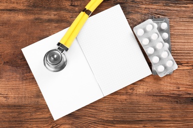 Photo of Stethoscope, open copybook and pills on wooden background. Heart attack concept