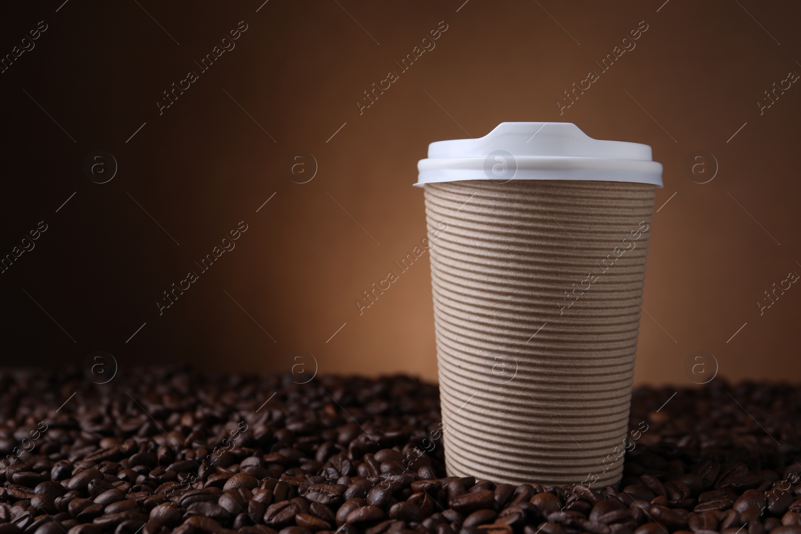 Photo of Coffee to go. Paper cup on roasted beans against brown background, space for text