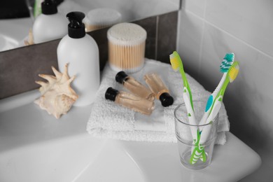 Photo of Colorful toothbrushes in glass holder and cosmetic products on washbasin