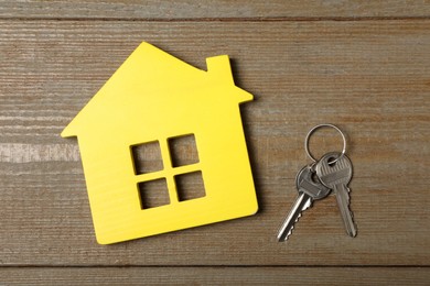 Photo of Yellow house model and keys on wooden table, flat lay. Housewarming party