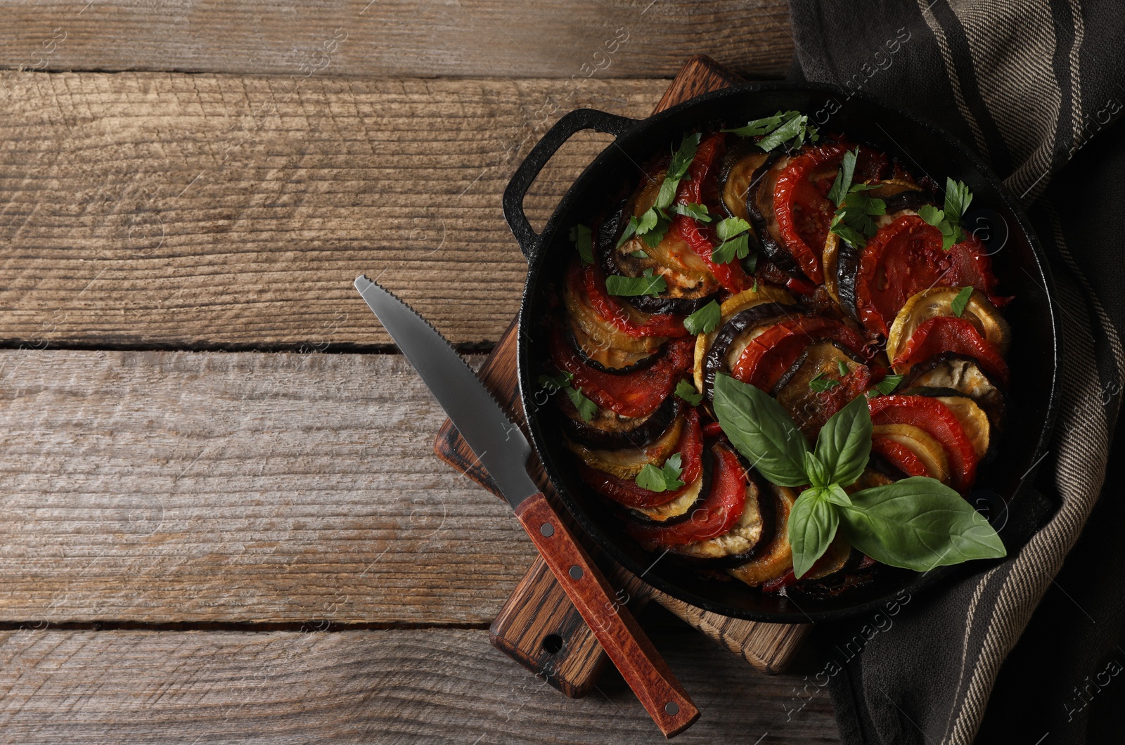 Photo of Delicious ratatouille and knife on wooden table, top view. Space for text