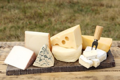 Photo of Different types of delicious cheeses on wooden table outdoors