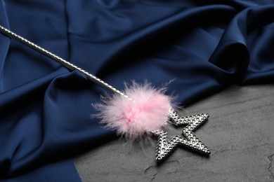 Photo of Beautiful silver magic wand with feather and blue fabric on black table
