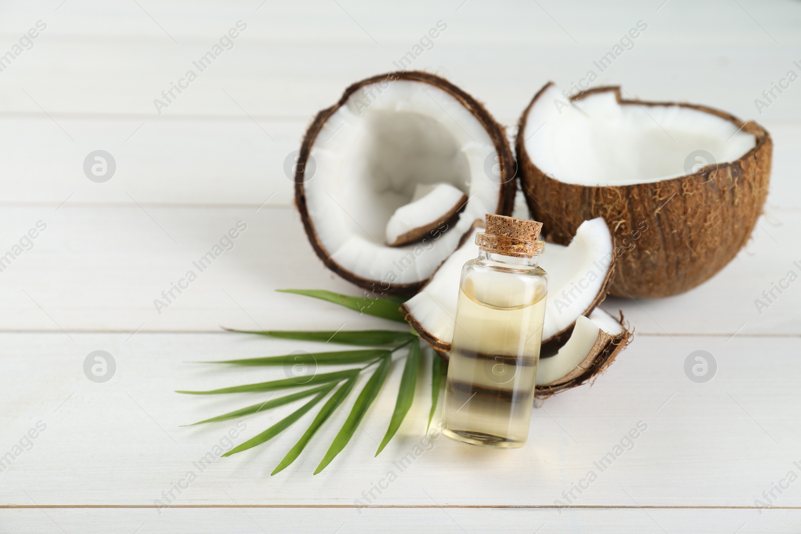 Photo of Bottle of organic coconut cooking oil, leaf and fresh fruits on white wooden table, space for text