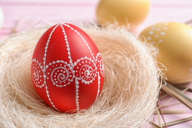 Photo of Nest with red painted Easter egg on table, closeup