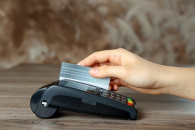 Photo of Woman with credit card using modern payment terminal at wooden table, closeup