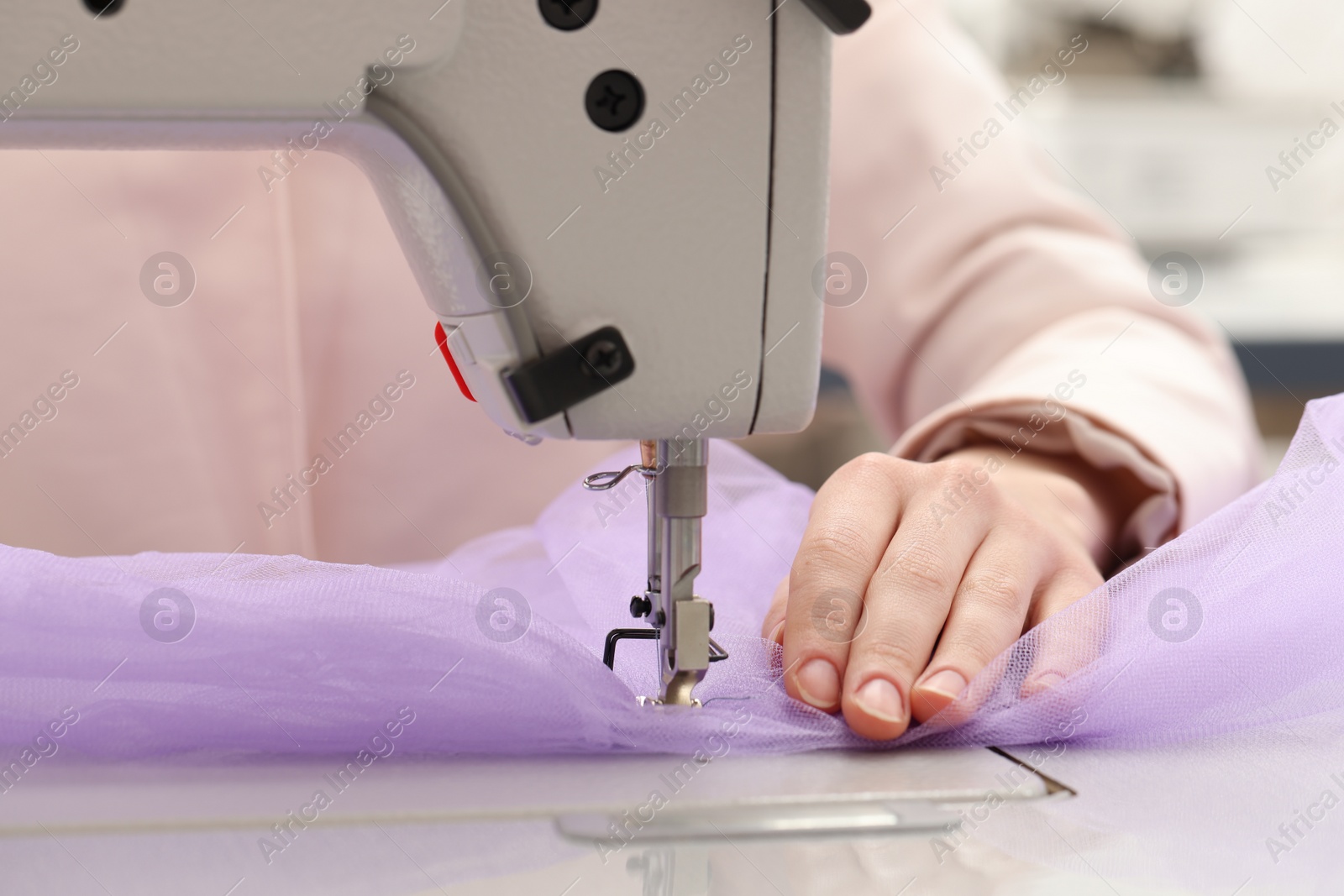 Photo of Dressmaker sewing new dress with machine in atelier, closeup