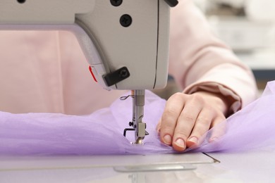 Photo of Dressmaker sewing new dress with machine in atelier, closeup