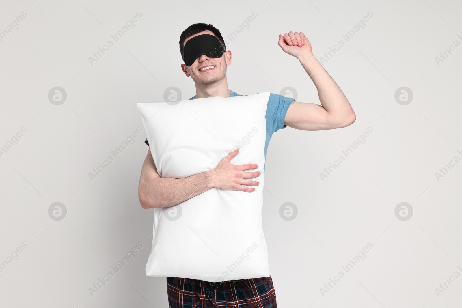 Photo of Happy man in pyjama and sleep mask holding pillow on light grey background