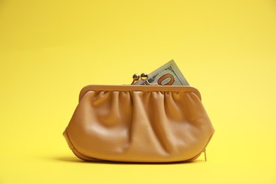 Photo of Stylish beige leather purse with dollar banknotes on yellow background