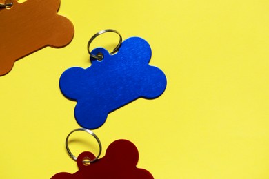 Color metal pet tags on yellow background, flat lay. Space for text