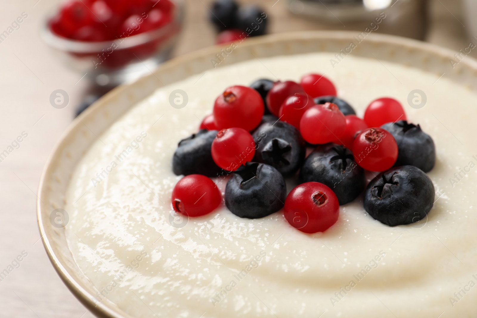 Photo of Delicious semolina pudding with berries in bowl on table, closeup