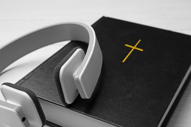 Photo of Bible and headphones on white table, closeup. Religious audiobook