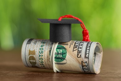 Photo of Scholarship concept. Graduation cap and dollar banknotes on wooden table, closeup