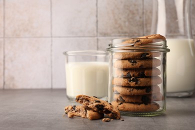 Photo of Glass jar with delicious chocolate chip cookies and milk on grey table. Space for text