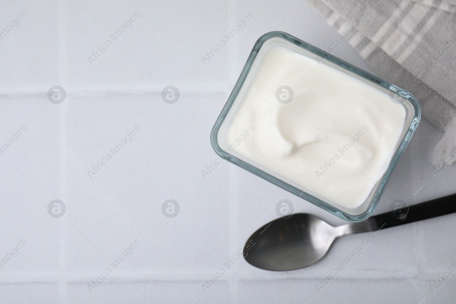 Photo of Delicious natural yogurt in bowl and spoon on white tiled table, top view. Space for text