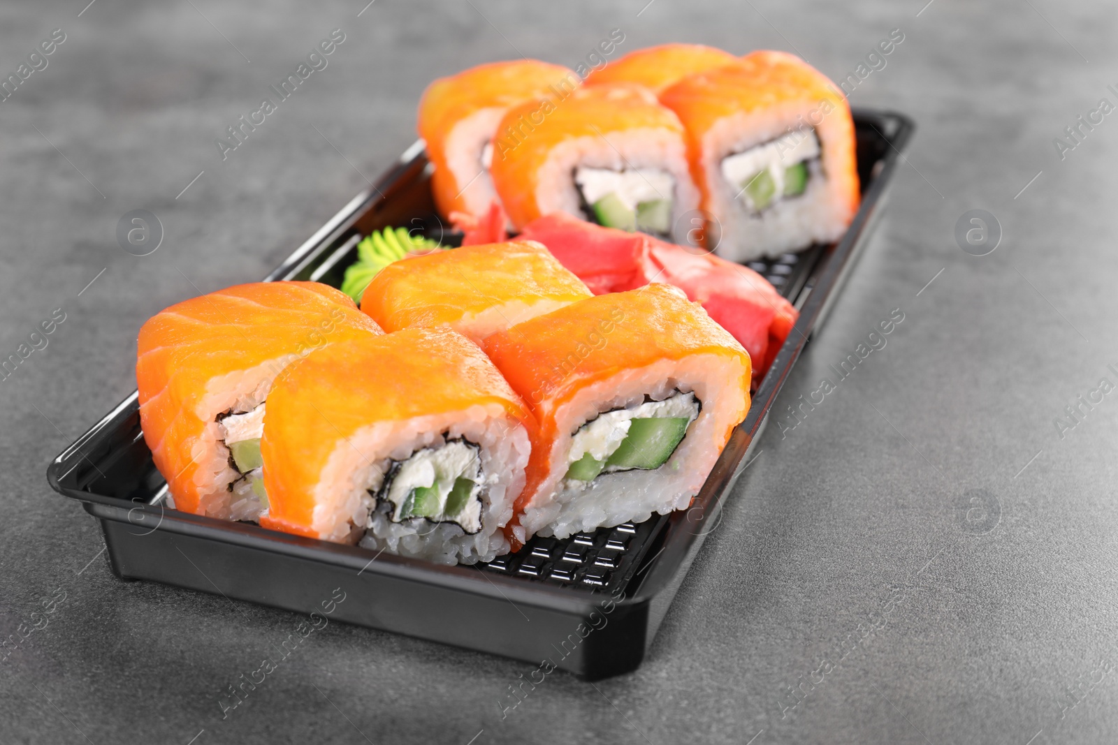 Photo of Box with tasty sushi rolls on grey table. Food delivery