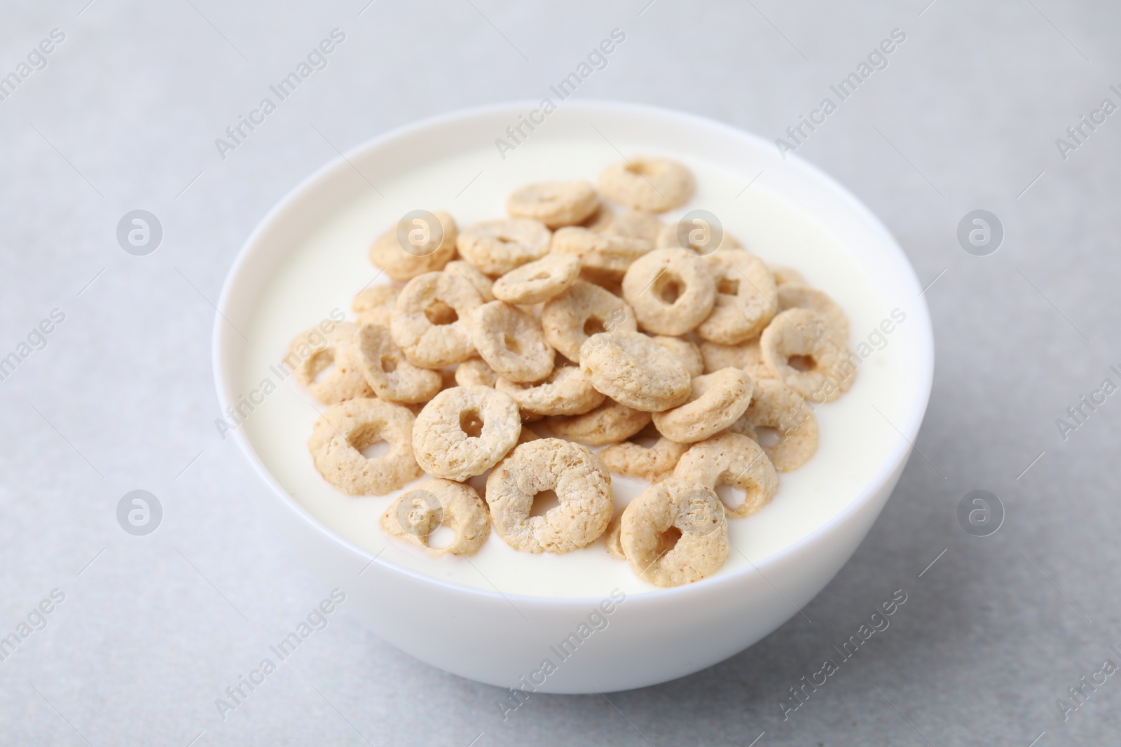 Photo of Breakfast cereal. Tasty corn rings with milk in bowl on grey table, closeup