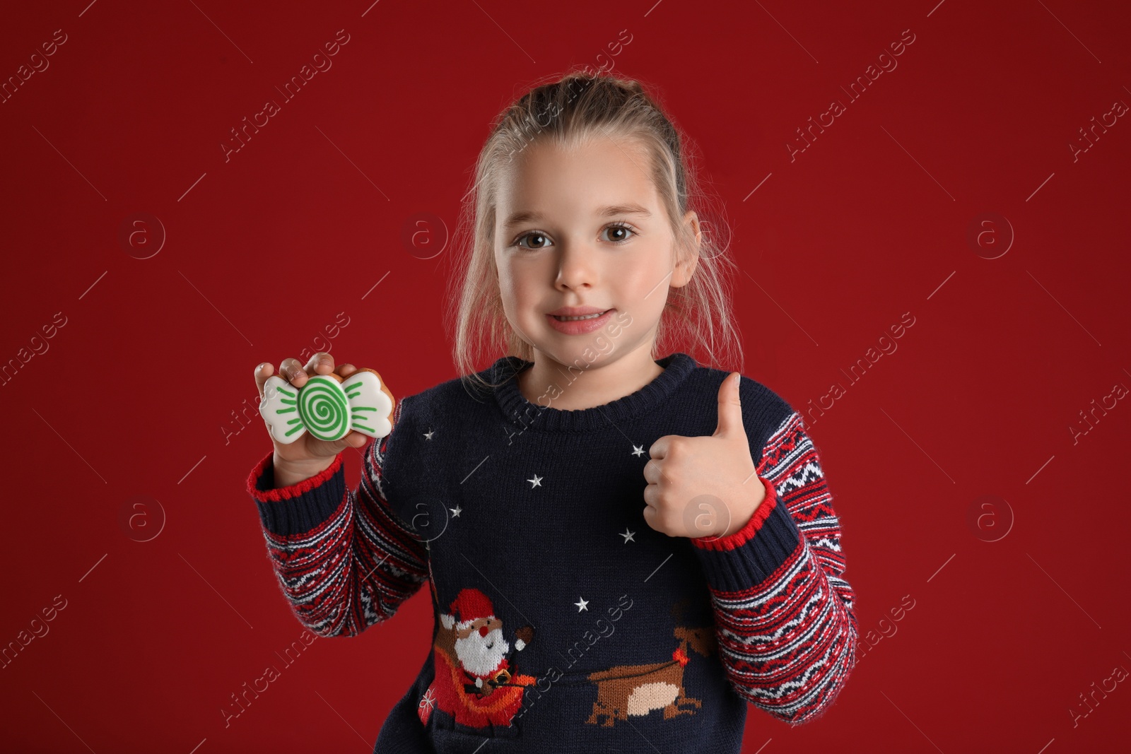 Photo of Cute little girl with Christmas gingerbread cookie on red background