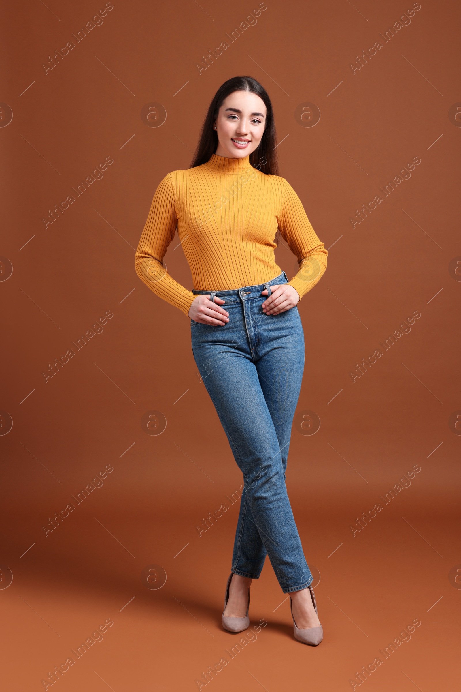 Photo of Young woman in stylish jeans on brown background