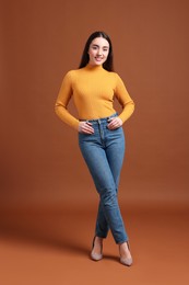 Young woman in stylish jeans on brown background