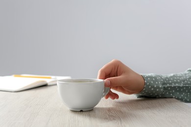 Photo of Woman with cup of drink at wooden table in office, closeup
