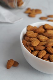 Photo of Bowl of delicious almonds on white marble table, closeup
