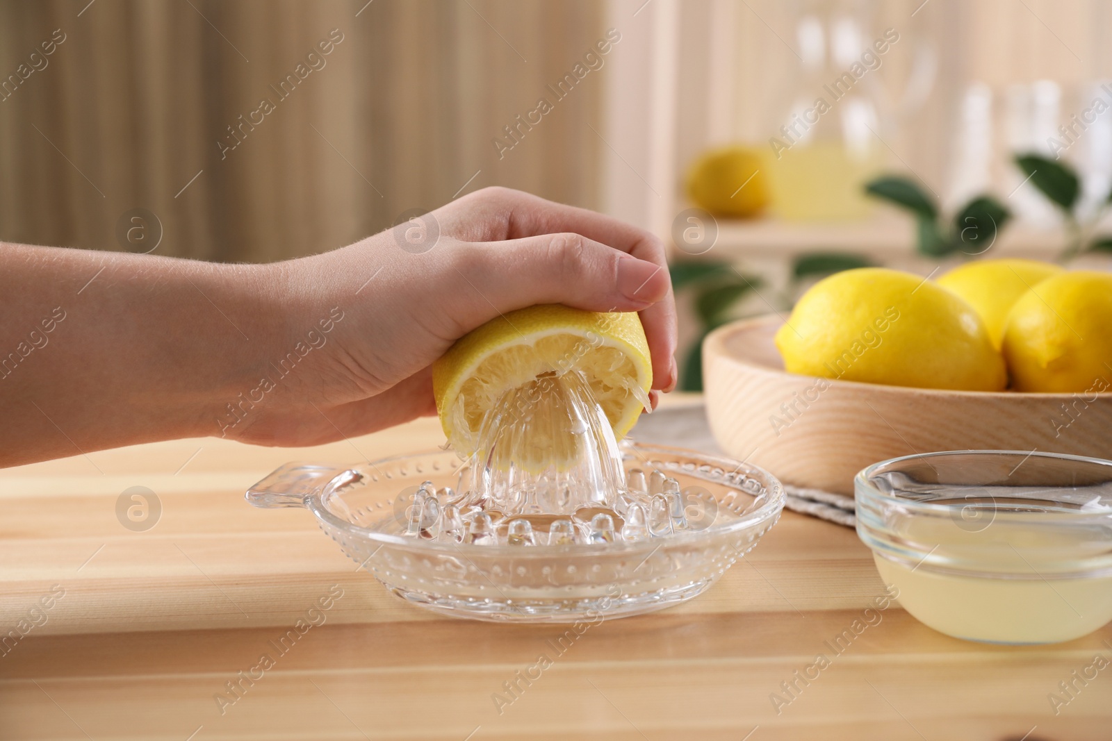 Photo of Woman squeezing lemon juice with reamer at wooden table, closeup