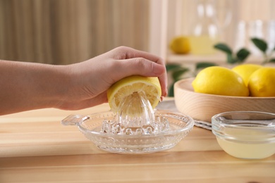 Woman squeezing lemon juice with reamer at wooden table, closeup