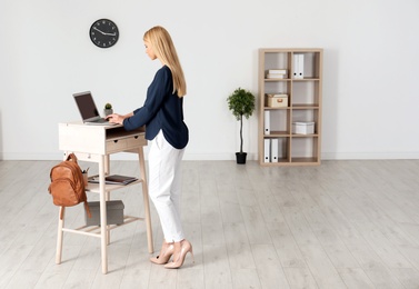Photo of Young woman using laptop at stand up workplace indoors