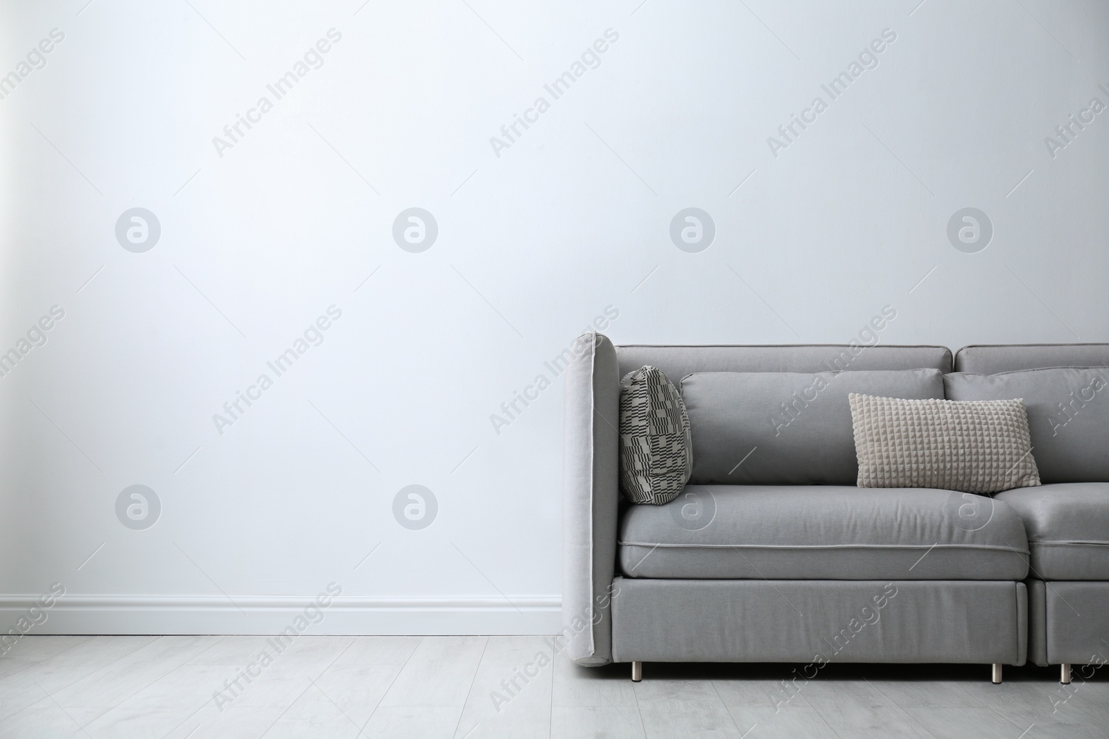 Photo of Grey sofa with pillows near white wall in stylish living room interior. Space for text