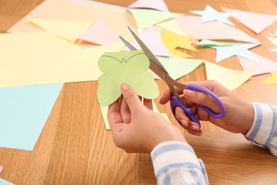 Photo of Woman cutting color paper with scissors at wooden table, closeup