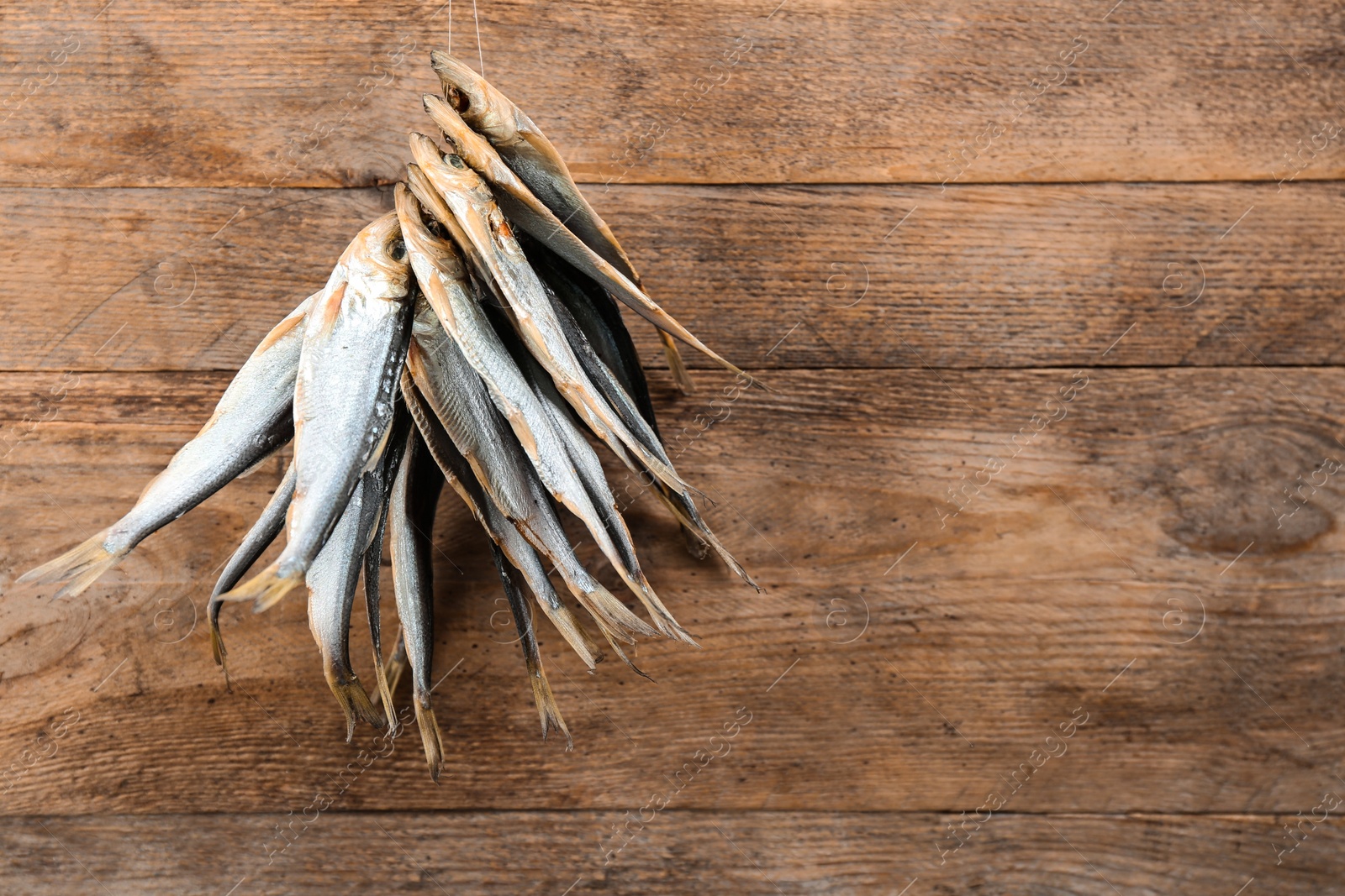 Photo of Dried fish hanging on rope against wooden background, space for text