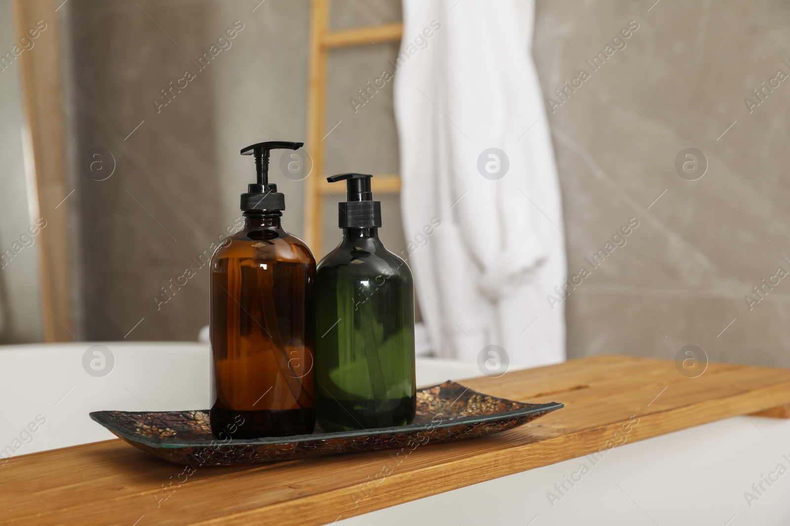 Photo of Wooden bath tray with bottles of shower gels on tub indoors, space for text