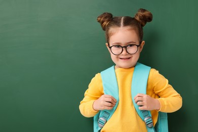 Photo of Happy little school child with backpack near chalkboard. Space for text