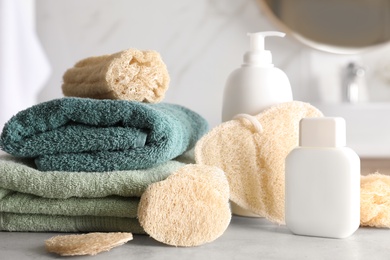 Photo of Natural loofah sponges, towels and cosmetic products on table in bathroom