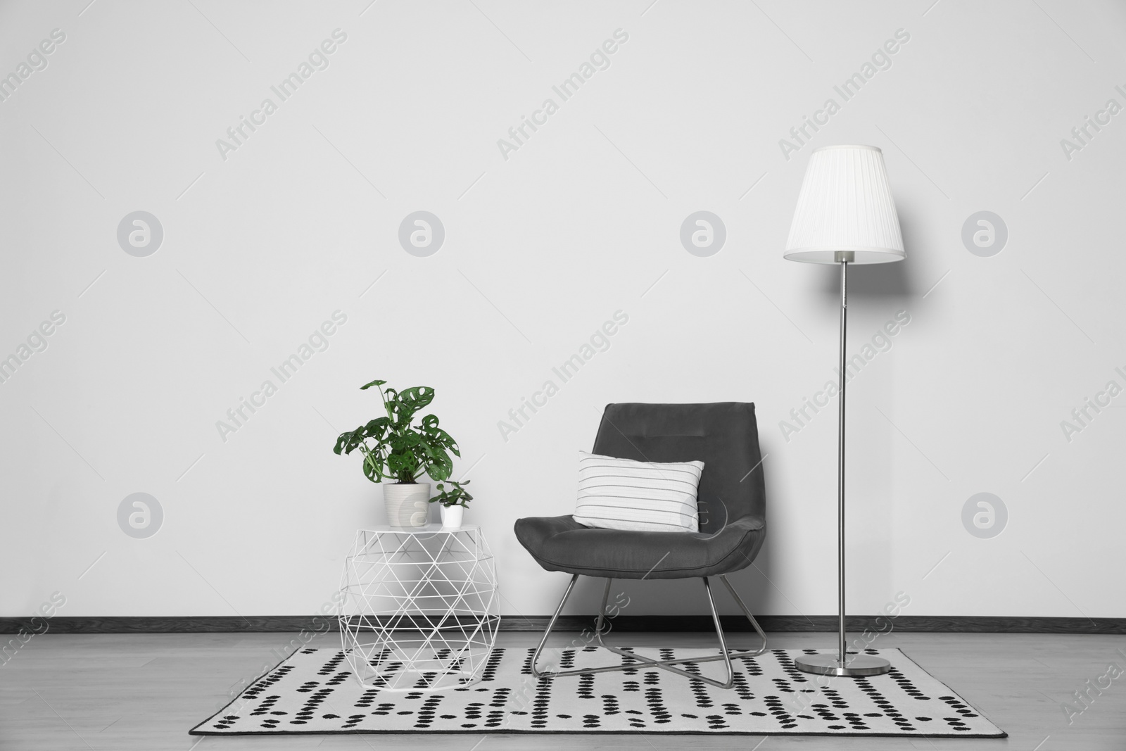 Photo of Stylish armchair, floor lamp and plants near white wall