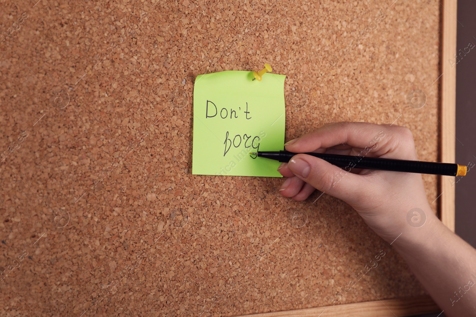 Photo of Woman writing paper note pinned to cork board, closeup