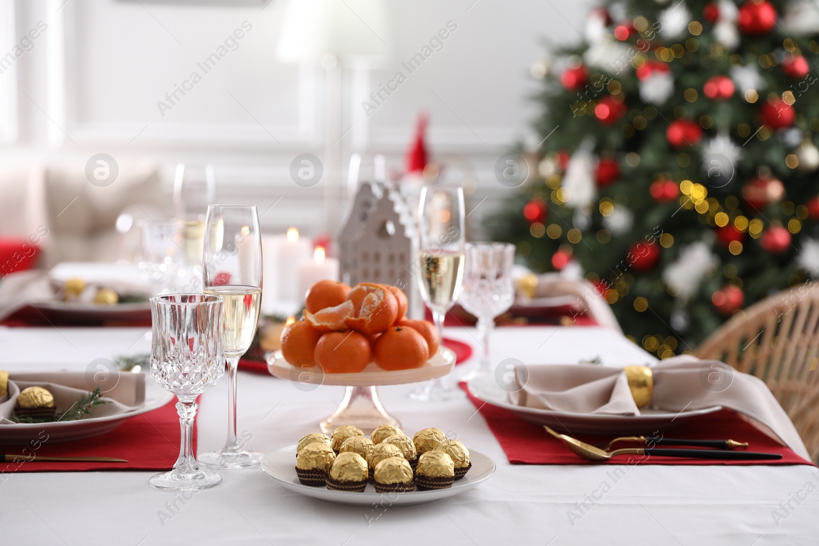 Photo of Christmas table setting with tangerines, candies and dishware indoors