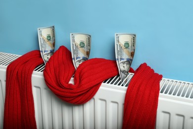 Photo of Modern radiator with knitted scarf and money near light blue wall indoors. Energy crisis concept