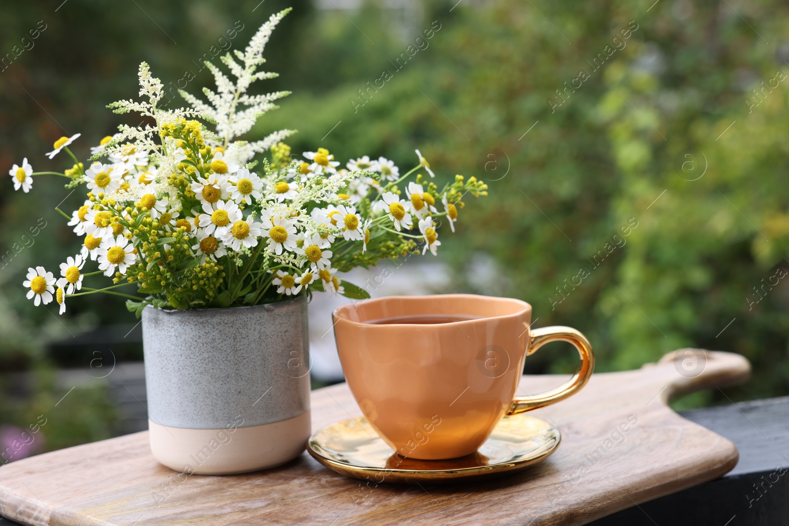 Photo of Cup of delicious chamomile tea and fresh flowers outdoors. Space for text