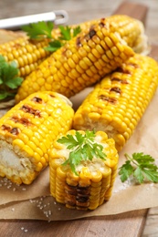 Photo of Delicious grilled corn cobs on wooden table, closeup